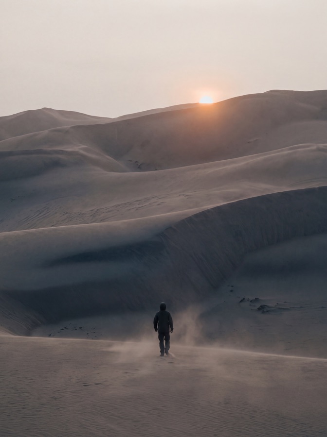 A lone figure crossing a dune field at dusk, dwarfed by the terrain.